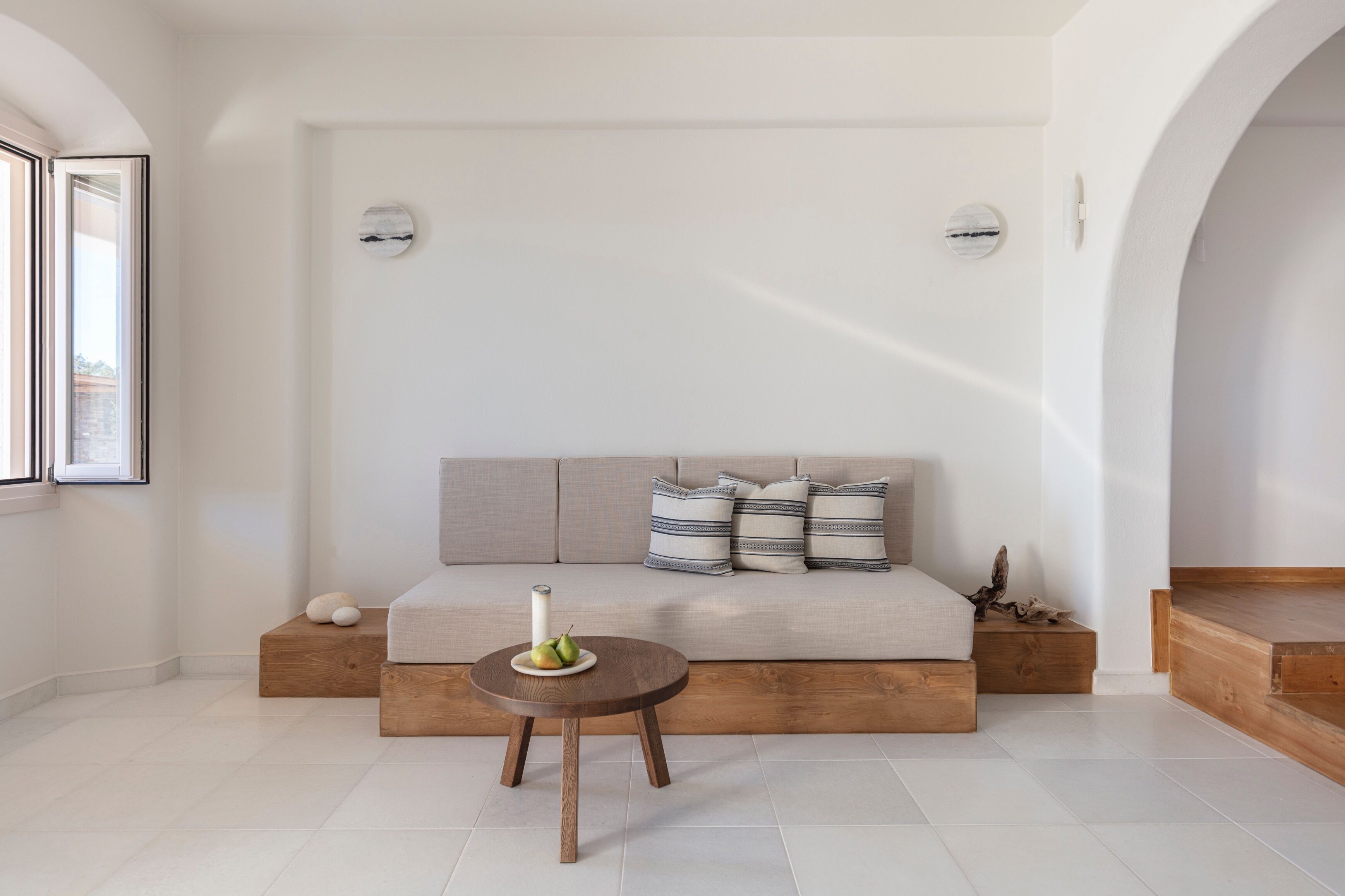 A modern living room with a sofa, a round wooden table with decorative items, and a minimalist design.