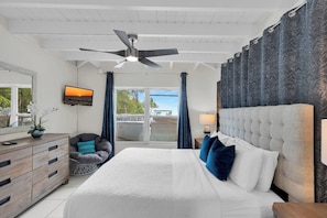 A bedroom with a bed, a ceiling fan, a TV, a dresser, a chair, and a view of the outdoors.