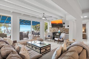 A spacious living area with a large TV, comfortable seating, and a view of the ocean. - The Lazy Lime – Spacious 5BR Retreat with Pool, Hot Tub & Open Water Views (Marathon)