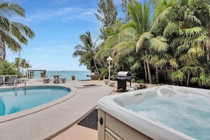 A pool area with a hot tub, lounge chairs, and a view of the ocean.