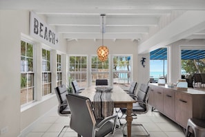 A spacious dining area with a large table, multiple chairs, and a view of the beach.