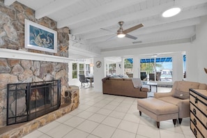 A spacious living area with a stone fireplace, a ceiling fan, and a view of the outdoors. - The Lazy Lime – Spacious 5BR Retreat with Pool, Hot Tub & Open Water Views (Marathon)