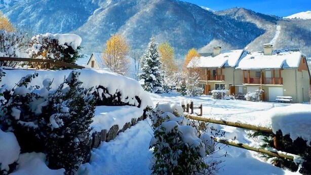 Un paysage montagneux enneigé avec un bâtiment doté d’un balcon et d’un toit recouvert de neige.