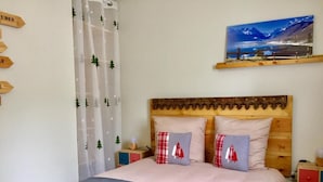 Une chambre à coucher avec une tête de lit en bois, deux tables de chevet, un lit recouvert d’une couverture grise et deux oreillers à motifs rouges et blancs.