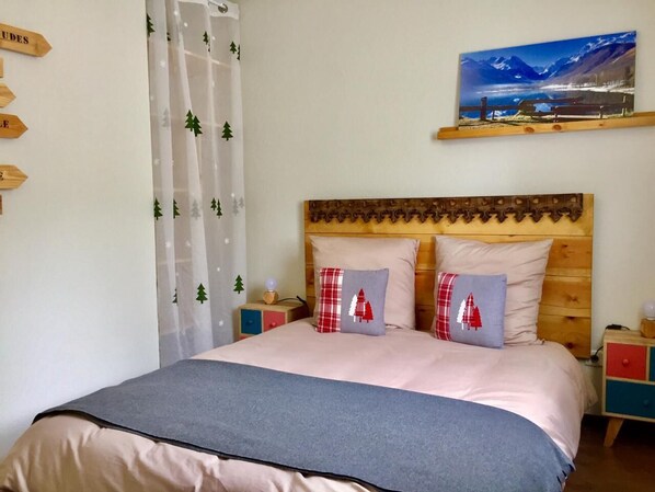 Ein Schlafzimmer mit einem hölzernen Kopfende, zwei Nachttischen, einem Bett mit grauer Decke und zwei Kissen mit roten und weißen Mustern.
