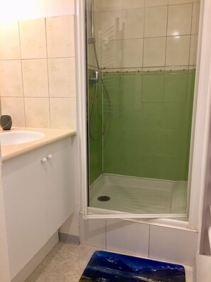 Ein Badezimmer mit einer grönen Duschkabine, einem weißen Waschbecken und einer kleinen, dunkel gefärbten Vase auf der Ablagefläche.