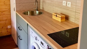 Une cuisine de taille réduite, équipée d’un lave-linge, d’un évier et de meubles de rangement en bois.
