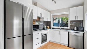 Una cocina moderna con electrodomésticos de acero inoxidable, armarios blancos y un ventanal que proporciona luz natural.