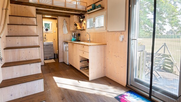 A wooden interior with a kitchen, a staircase, and a large sliding glass door to the outside. - Tiny house on the alpaca farm - Tiny House (Rubkow)