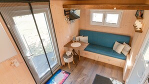 A cozy cabin interior with a wooden floor, a blue sofa, a small table, and a TV mounted on the wall. - Tiny house on the alpaca farm - Tiny House (Rubkow)