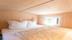 A bedroom with a wooden ceiling, a window, and a bed with white bedding. - Tiny house on the alpaca farm - Tiny House (Rubkow)