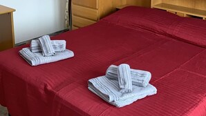 A hotel room with a red bedspread, two neatly folded towels, a wooden wardrobe, and a small wooden table. - House at Nonna Pina's at the gateway to the Val Grande (Cossogno)