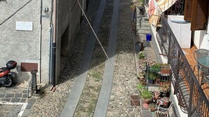A narrow street flanked by traditional buildings with tiled roofs, a paved path, and a mountainous backdrop. - House at Nonna Pina's at the gateway to the Val Grande (Cossogno)