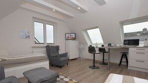 Una habitación moderna y bien iluminada con una cama, sillones grises, un escritorio pequeño y una zona de cocina con microondas.