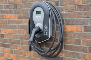 A charging station with a digital display and a cable connected to it, mounted on a brick wall.