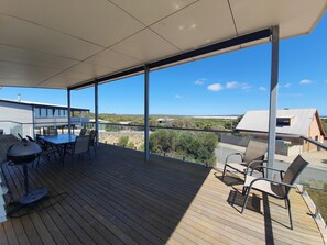 A covered outdoor deck with a table and chairs, overlooking a residential area and natural landscape.