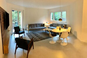 A modern living room with a sofa, chairs, a dining table, and a TV. - Coloratura (Paradiso)