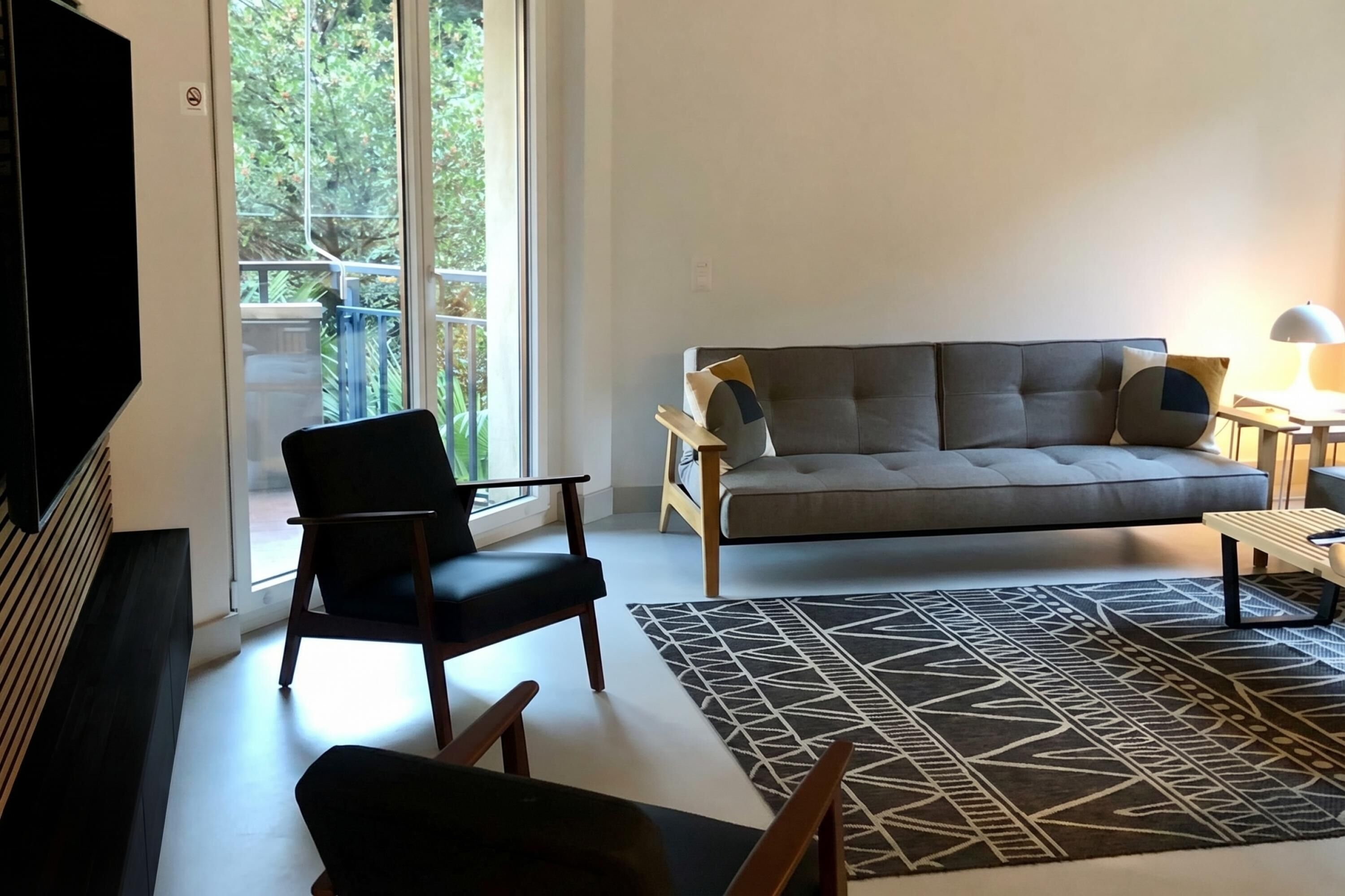A living room with a sofa, chairs, a TV, and a patterned rug.