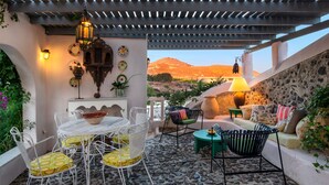 A patio with a stone floor, white metal furniture, and a view of a mountain. - Hiraeth: Stylish canava house with pool and garden (Μεγαλοχώρι)