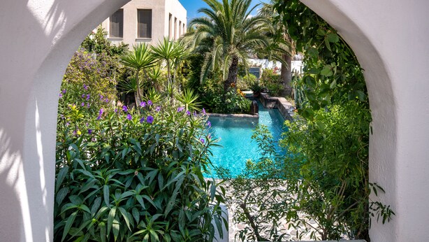 A pool surrounded by lush greenery and a white archway. - Hiraeth: Stylish canava house with pool and garden (Μεγαλοχώρι)