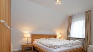 A neatly made bed in a hotel room with wooden flooring, two bedside lamps, and a window with curtains. - A 2 GH 2-room balcony (BC.n5) - Stranddomicil Steiner - Guesthouses (Büsum)