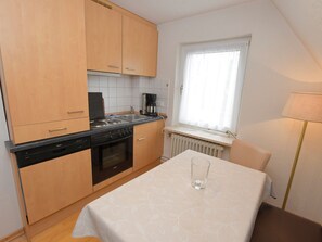 A compact kitchen with wooden cabinets, a Bosch dishwasher, a stove, and a window with a white curtain. - A 2 GH 2-room balcony (BC.n5) - Stranddomicil Steiner - Guesthouses (Büsum)