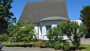 A house with a tiled roof, a circular front porch, and a garden with various plants and flowers. - A 2 GH 2-room balcony (BC.n5) - Stranddomicil Steiner - Guesthouses (Büsum)