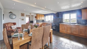 A modern kitchen with wooden cabinets, a dining area with wicker chairs, and a large clock on the wall.