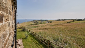 A stone building with a view of a rural landscape, including fields and distant houses.