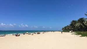 Une plage avec un ciel dégagé, des palmiers et des gens qui se détendent.