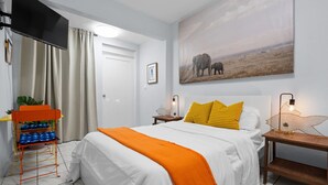 Une chambre à coucher avec un lit, une télévision, un tableau et une table de chevet avec une lampe.