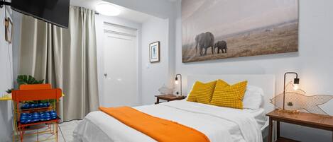 A bedroom with a bed, a TV, a painting, and a nightstand with a lamp.