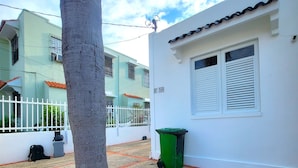 Zona residencial amb un edifici blanc, un arbre, un safataig verd i una tanca blanca.