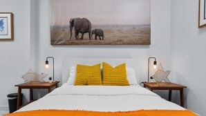 Un dormitori amb un llit gran, dues tauletes de nit, un quadre amb elefants i una làmpada amb forma d'estrella a cada tauleta.