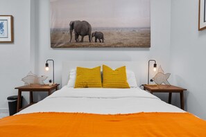 Ein Schlafzimmer mit einem großen Bett, zwei Nachttischen, einem gerahmten Bild von Elefanten und einer sternförmigen Lampe auf jedem Nachttisch.