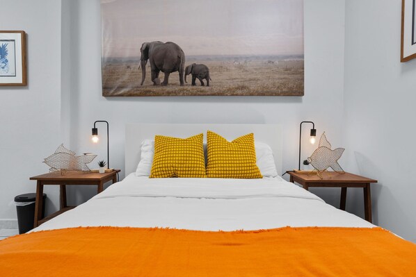 A bedroom with a large bed, two nightstands, a framed picture of elephants, and a star-shaped lamp on each nightstand.