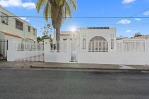 A gated residential area with a white fence, a palm tree, and a clear sky.