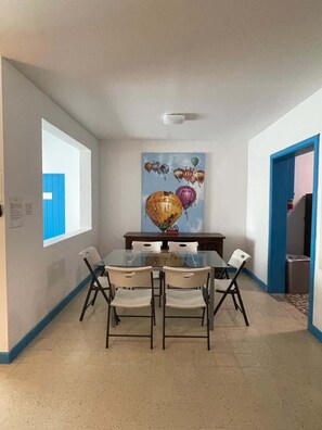 Un coin repas avec une table et des chaises en verre, une porte à cadre bleu et un tableau représentant des montgolfières accroché au mur.