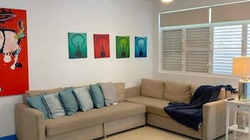 A living room with a beige sectional sofa, a ceiling fan, and four light bulb paintings on the wall.