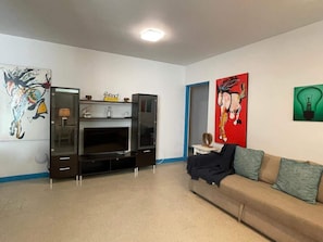 Una sala de estar con televisor, sofá y obras de arte en las paredes.