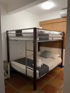 Dormitorio con literas, una mesita pequeña y aire acondicionado instalado en la pared.