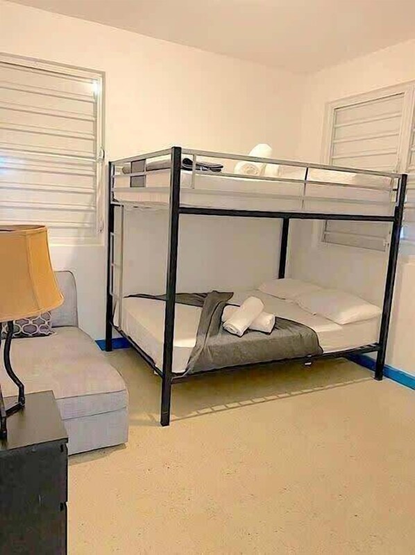 A bunk bed with a desk and chair, a lamp, and a window with blinds.