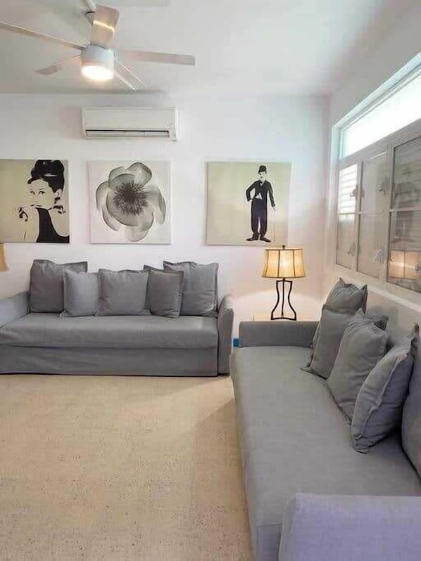 A living room with a grey sofa, a side table with a lamp, and artwork on the wall.