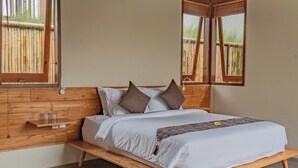 A bedroom with a wooden bed frame, white bedding, and two windows with wooden frames.
