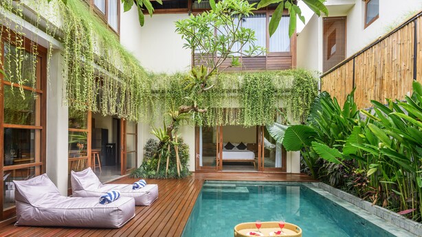 A modern outdoor pool area with wooden deck seating and lush greenery.