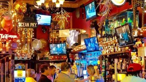 Eine Bar mit mehreren Fernsehern, einer Auswahl an Flaschen und einer Holztresen.