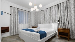 Ein modernes Schlafzimmer mit einem großen Bett, einem Nachttisch, einer Wandlampe und gemusterten Vorhängen.