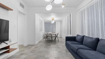 En moderne stue med et fladskærms-TV, en mørk sofa, et spiseområde med bord og stole, og et gulv med et mønster.