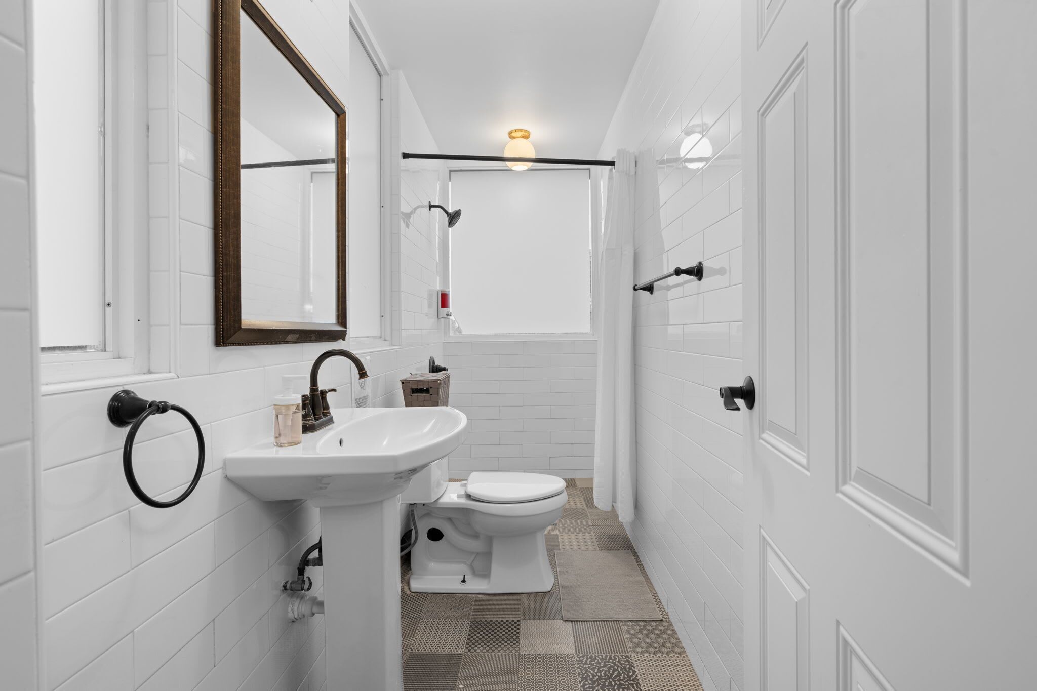 Une salle de bain avec des murs recouverts de carreaux blancs, un lavabo, des toilettes, un miroir et un espace douche.