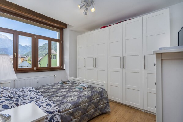 A bedroom with a bed, a window with a view of mountains, and a wardrobe.